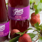 Two bottles of Glam Food plum and raspberry splash on a white surface with plums and green leaves.